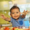 A baby happily plays with colorful toys in a bright and cheerful playroom. The baby is reaching out.
