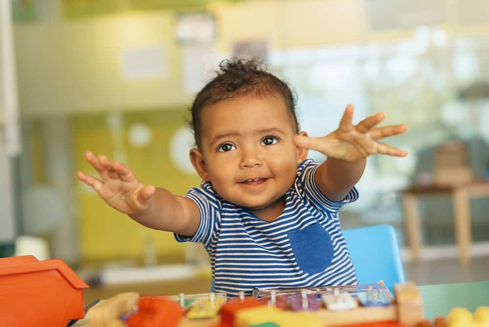A baby happily plays with colorful toys in a bright and cheerful playroom. The baby is reaching out.