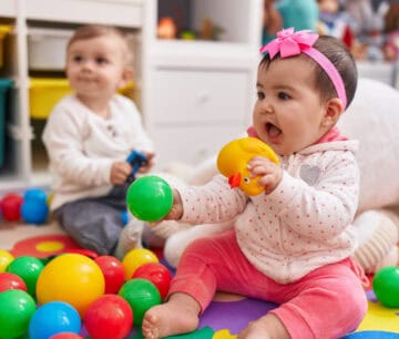 Adorable boy and girl playing with balls sitting on floor at kindergarten