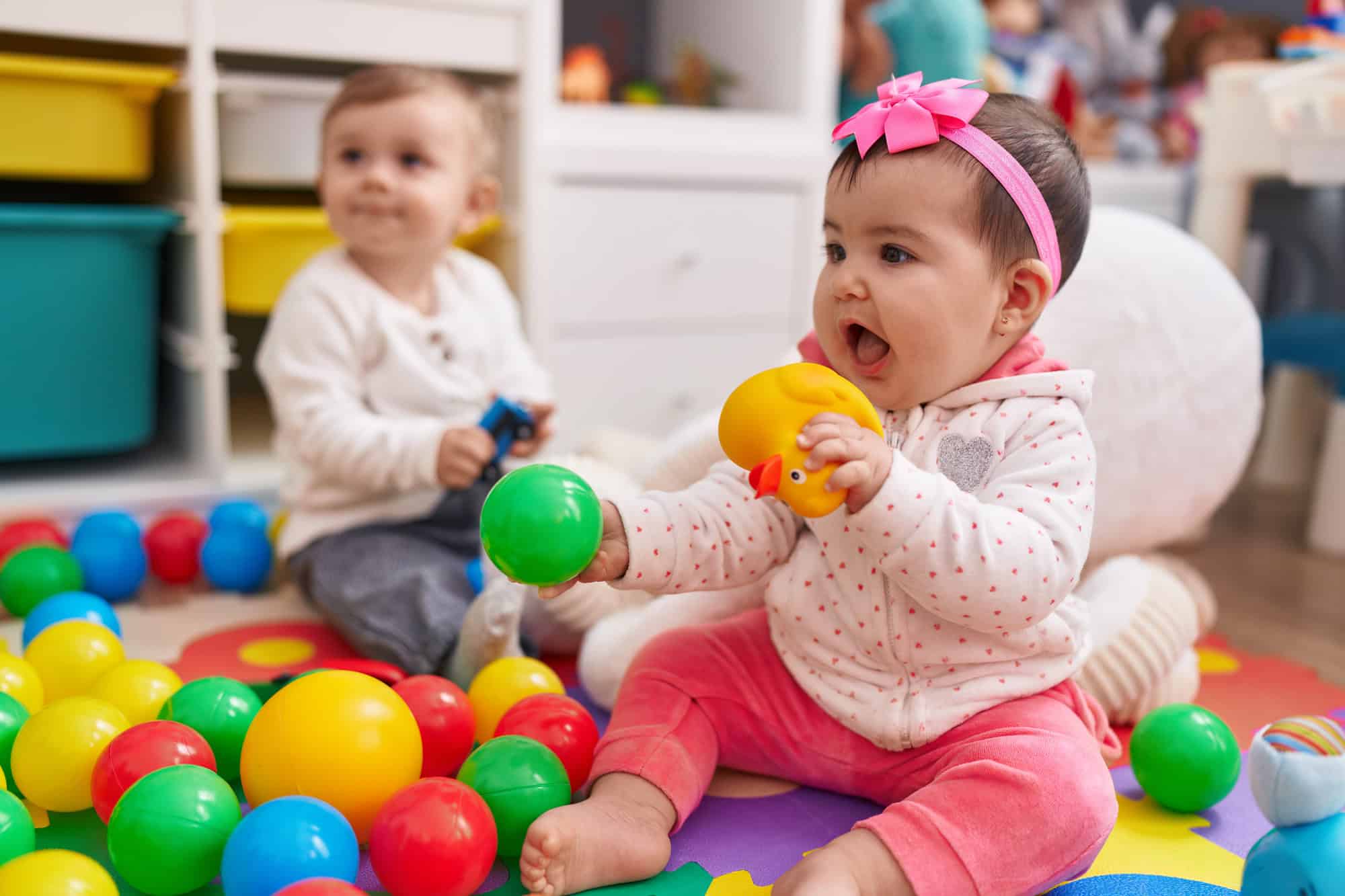 Adorable boy and girl playing with balls sitting on floor at kindergarten